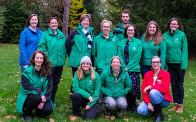 A group of people smiling at the camera on the grass with trees in the background