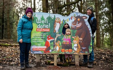 Family wearing winter clothes gathered around a Gruffalo sign