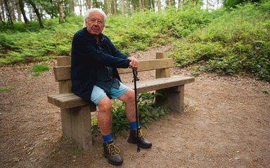 Man sitting on a bench in a forest with a walking stick