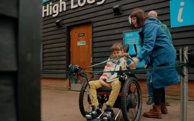 A young girl in a wheelchair pulls a ceremonial ribbon, accompanied by her mother.