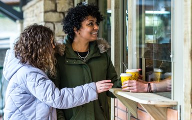 A woman and a girl accepting coffees from a coffee shop window