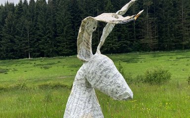 A sculpture of a hare made out of music sheets placed in the forest