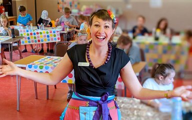 A photograph of a person leading a craft activity in a classroom full of children