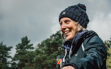 A smiling woman wearing coat and woolly hat.