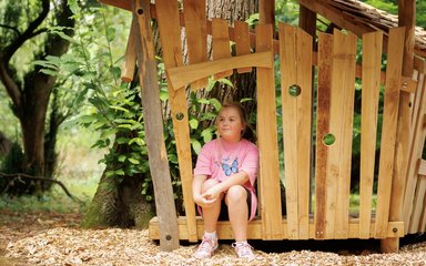 a girl sits inside a small wooden hut looking content