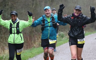 3 people smiling and running in the forest, in wet conditions