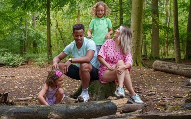 Two adults and two children in summer clothes sitting among logs and branches in the forest