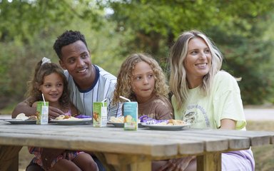 Two parents and two children sitting at a picnic bench with plates of food and drinks