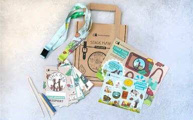 Flat lay showing lanyard, activity cards, pencil, pipe cleaner, stickers and branded Stick Man paper bag