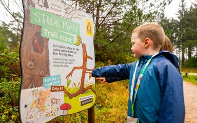 Two children in the forest pointing to a Stick Man branded panel