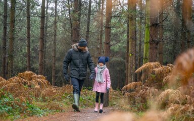 A man and girl in winter coats and hats walk on a forest path