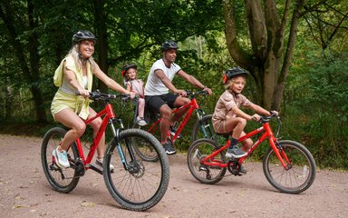 Two adults and two children all riding red bikes on a forest path