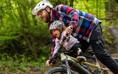 A man on a mountain bike with a smiling toddler seated with him on a child seat.