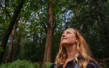 Woman in the forest, looking up into the trees.