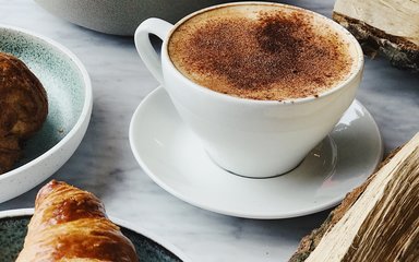 A cappuccino and croissant on a table with pieces of chopped logs
