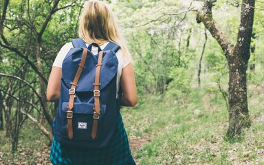 Women with blue backpack walking through spring woodland