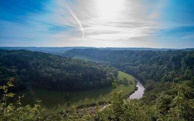 Looking down to a river winding through lush green landscape, against a blue sky.