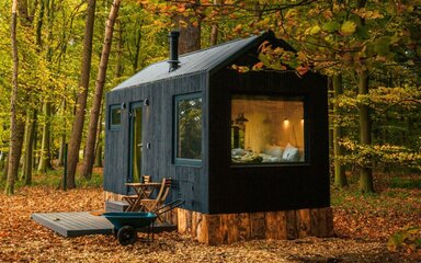 A small and cosy-looking off-grid cabin lit up in autumn woodland.
