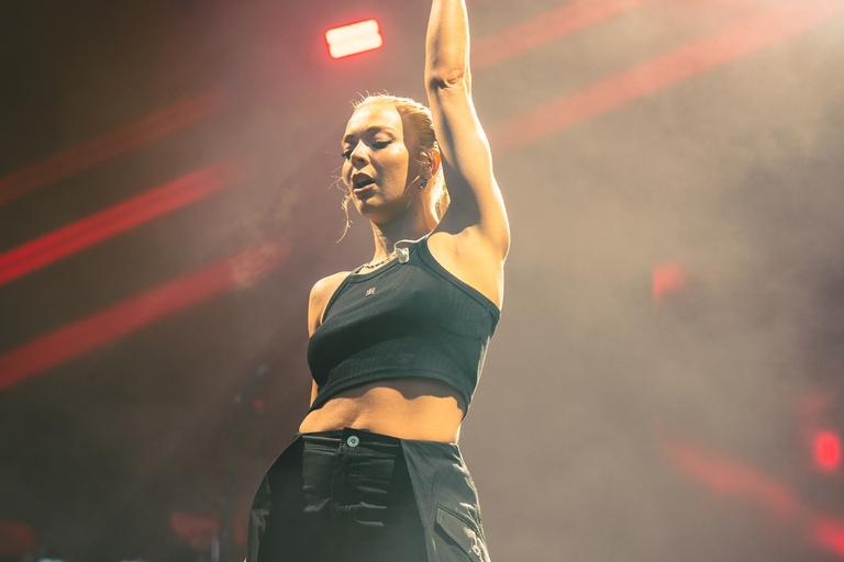 Close-up of female singer Becky Hill on stage, with one arm high in the air.