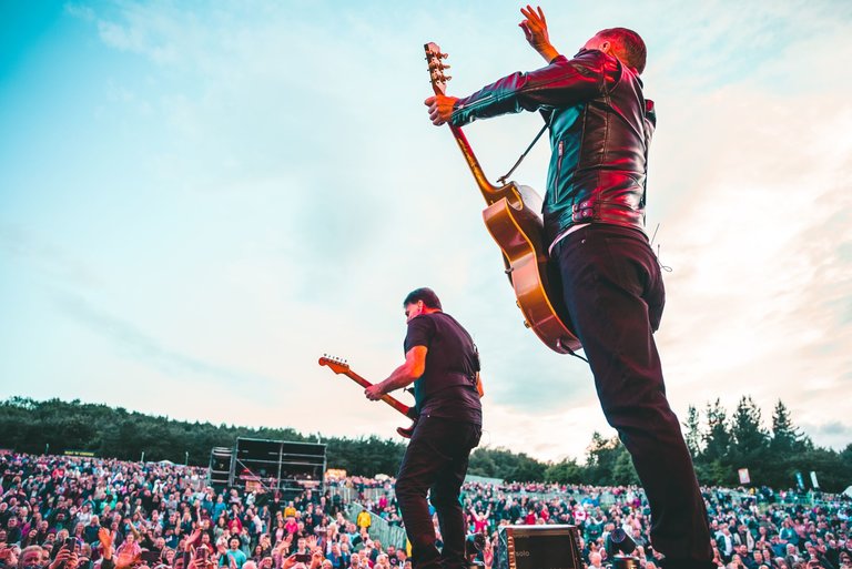 Male singer Bryan Adams, from behind, on stage holding a guitar with a large crowd in view.