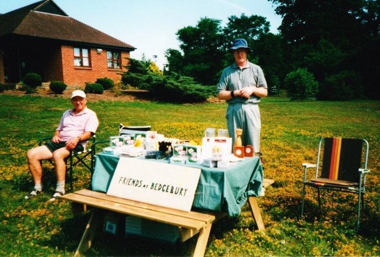 An old colour photograph showing two men at bench with a handmade sign saying Friends of Bedgebury