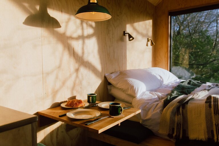 Unyoked off grid cabin inerior with unmade bed and side table with food