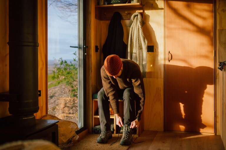 Unyoked cabin interior with a man sitting on a bench putting on walking boots