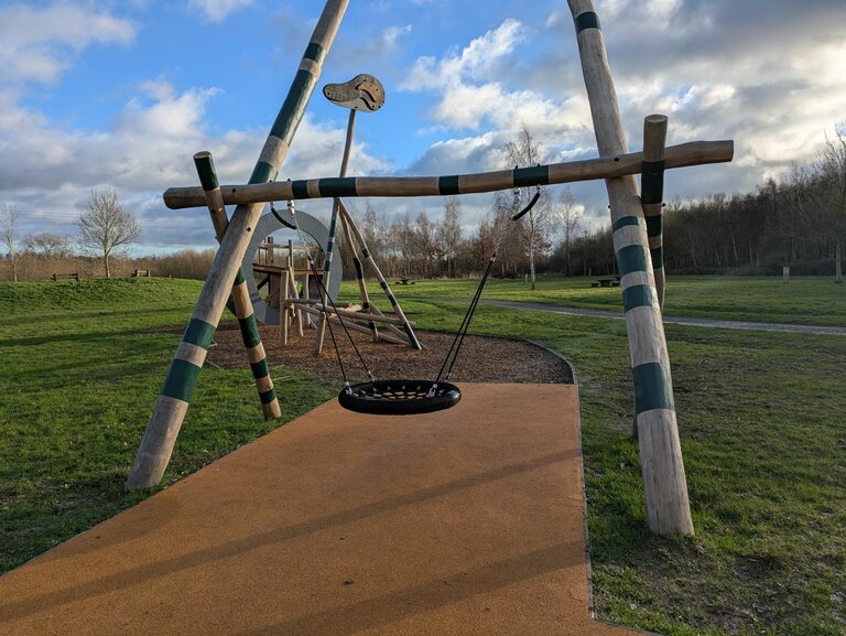 A basket swing on a wooden frame in an outdoor setting.