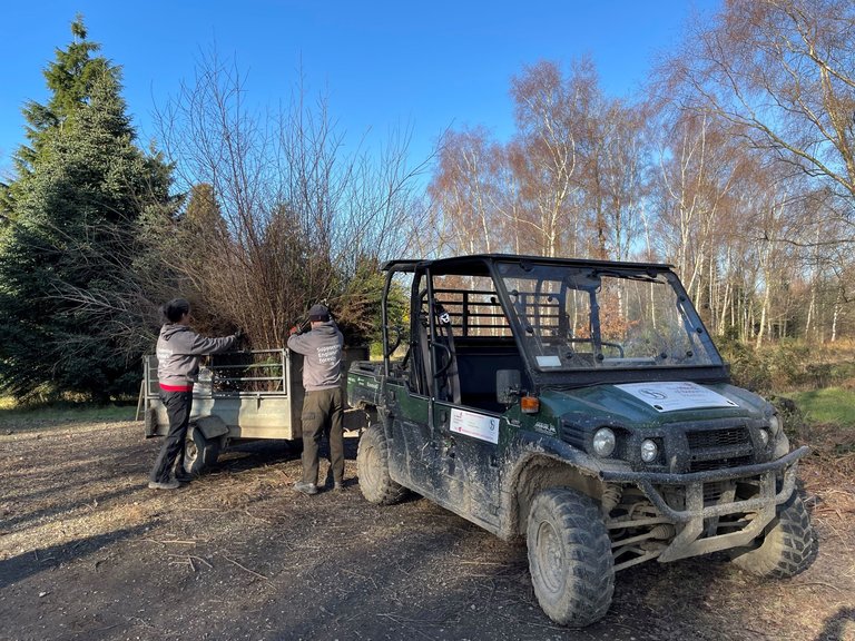 Two volunteers loading cuttings into a trailer attached to a muddy vehicle.